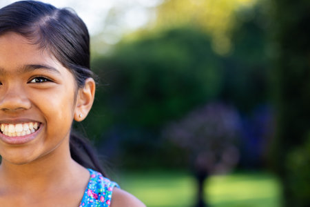 Outdoors, young biracial girl smiling brightly with colorful dress, copy space. She is in lush green background, enjoying fresh air and vibrant surroundings, unalteredの写真素材