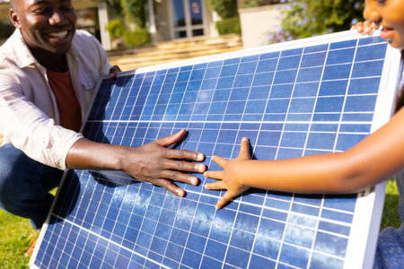 Outdoors, diverse father and daughter touching solar panel together. Outside in sunny yard with a house in background, sharing a moment of learning and discovery, unalteredの写真素材