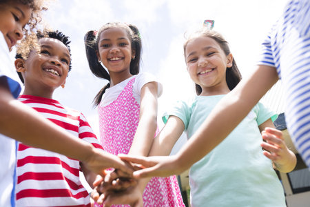 In school, diverse students are joining hands together outside. They are wearing colorful casual clothes and smiling under bright sky, unalteredの写真素材
