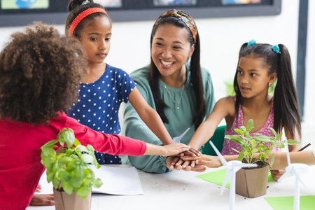 A biracial female teacher with students gathered around table with plants. They are in bright classroom, engaging in a hands-on learning activity about nature, unalteredの写真素材