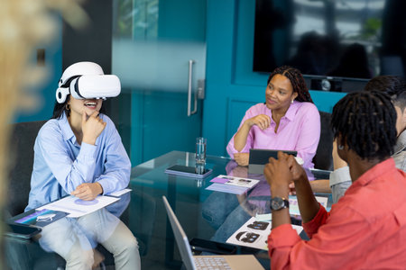 Business team collaborate in a startup, one using a VR headset, showcasing teamwork. They are in modern office with glass walls and a large screen in background, unalteredの写真素材