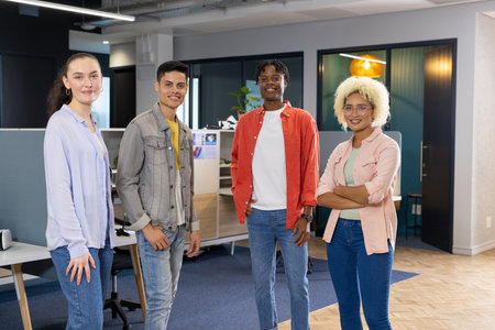 Diverse Business colleagues standing together in a modern office, showcasing teamwork. Open workspace with desks and computers in background, creating collaborative environment, unalteredの写真素材