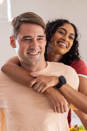 Diverse couple embracing and smiling warmly. Bright, cozy indoor setting with soft lighting creating relaxed atmosphere, unalteredの写真素材