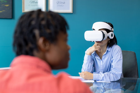 Asian woman uses VR headset while African American man observes, startup business teamwork. They are...