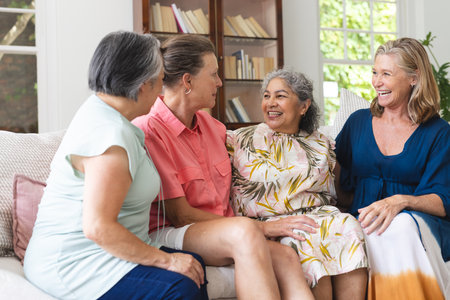 Diverse, mature women sitting together, smiling in living room at home. retirement, friendship, senior living, happiness. sharing stories and enjoying each other's company, unalteredの写真素材