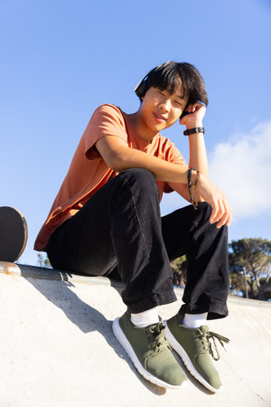 Listening to music with headphones, Asian teenage boy sitting at skatepark. leisure, relaxation, unalteredの写真素材