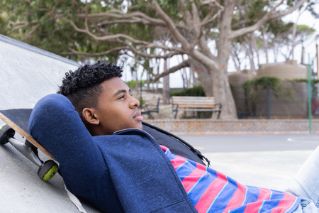 Relaxing at skatepark, teenage boy lying on skateboard, enjoying leisure time. Skateboarding, relaxation, teenage lifestyle, outdoors, unalteredの写真素材