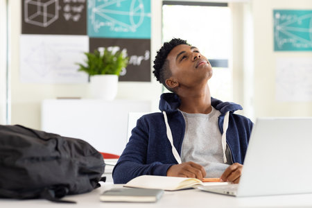 In school, African American male student sitting at desk with laptop, looking thoughtful, copy space. Education, technology, learning, classroom, unalteredの写真素材