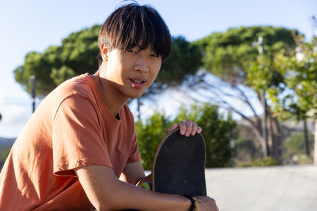 Holding skateboard, Asian teenage boy relaxing outdoors in skate park, copy space. Skateboarding, youth, recreation, leisure, urban, unalteredの写真素材