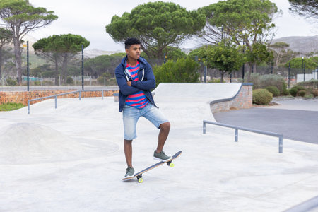 Skateboarding in park, teenage boy standing on skateboard, enjoying outdoor activity. recreation, youth, lifestyle, sports, unalteredの写真素材