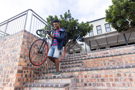 Carrying bicycle down stairs, African American male student in casual clothes outdoors, copy space. Transport, mobility, urban, male student life, outdoor activity, independence, unalteredの写真素材