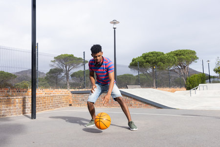 Playing basketball outdoors, man dribbling ball on court in casual attire. Sports, athletic, exercise, competition, game, activity, unalteredの写真素材