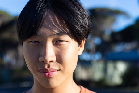Asian male student smiling outdoors, enjoying leisure time in natural setting. Youth, happiness, greenery, freedom, relaxation, unalteredの写真素材