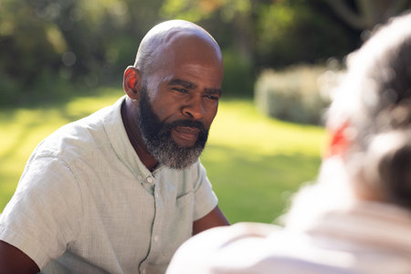 Talking with friend outdoors, man enjoying conversation in sunny garden. Friendship, socializing, leisure, relaxation, communication, nature, unalteredの写真素材
