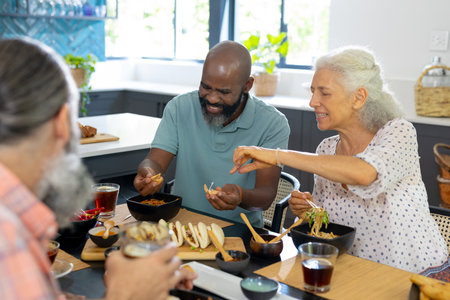 Eating together, diverse group of senior friends enjoying meal at home. Seniors, friendship, dining, socializing, diversity, unalteredの写真素材