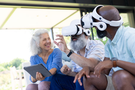 At home, Senior friends using VR headsets and tablet, enjoying virtual reality experience. Technology, seniors, friendship, leisure, innovation, unalteredの写真素材