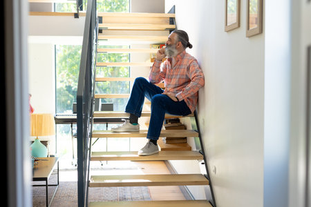 Sitting on stairs, senior man drinking coffee and looking out window at home. relaxation, morning, unalteredの写真素材