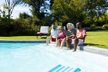 Group of senior friends sitting by pool, enjoying sunny day together. seniors, leisure, poolside, relaxation, summer, outdoors, unalteredの写真素材