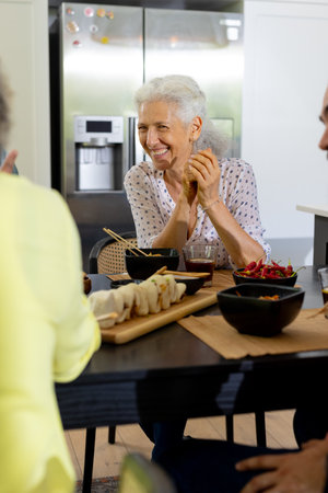 At home, Smiling senior woman enjoying meal with friends at dining table in kitchen. Friendship, togetherness, happiness, elderly, lifestyle, unalteredの写真素材
