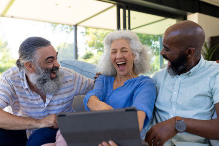 At home, Diverse group of friends laughing and watching something on tablet together. Friendship, technology, leisure, togetherness, bonding, entertainment, unalteredの写真素材