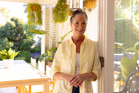 Smiling senior woman standing in bright home with plants and natural light. Lifestyle, happiness, indoors, greenery, relaxation, casualの写真素材