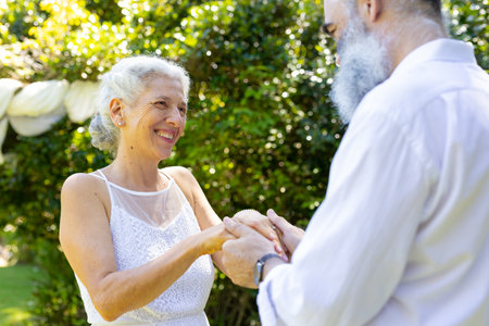 Smiling senior bride holding hands with groom at outdoor wedding. Elderly, happy, couple, affection, relationship, cheerfulの写真素材