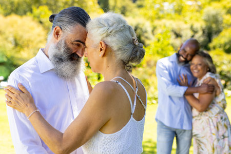 Senior bride and groom dancing and embracing at outdoor wedding, enjoying time together in park. Elderly, love, happiness, joyful, retirement, leisureの写真素材