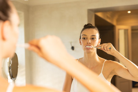 Brushing teeth, woman looking in mirror in bathroom, focusing on oral hygiene. dental, morning routine, self-care, clean, reflection, dental careの写真素材