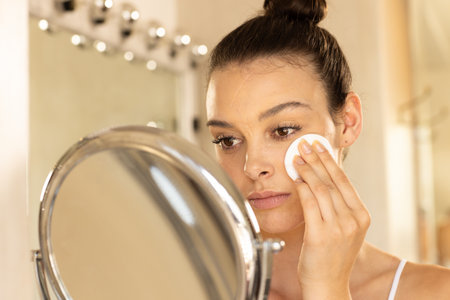 Applying makeup, young woman using cotton pad in front of mirror. Beauty, skincare, cosmetics, routine, self-care, hygieneの写真素材
