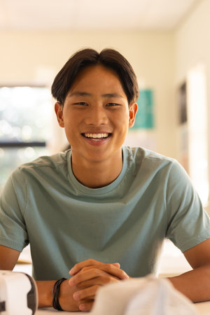Smiling teenage boy sitting at high school desk, looking at camera in classroom. Education, student,...