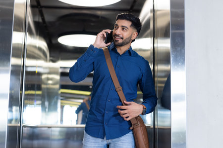 Talking on smartphone, man with messenger bag smiling in elevator. Business, communication,...