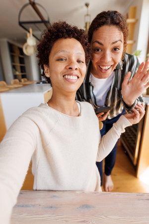 Happy diverse lesbian couple having video call. Spending quality time at home, technology, domestic life and lifestyle concept.の写真素材