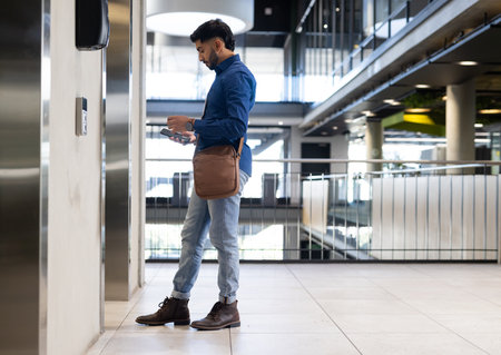 Businessman using smartphone and waiting for elevator in modern office building, copy space....