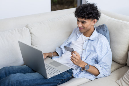 Shopping online, young man holding credit card and using laptop on couch. E-commerce, online shopping, internet, payment, transaction, digitalの写真素材