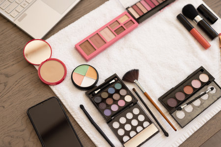Makeup products and smartphone on table, ready for beauty routine at home. Cosmetics, skincare, lipstick, foundation, eyeshadow, glossの写真素材