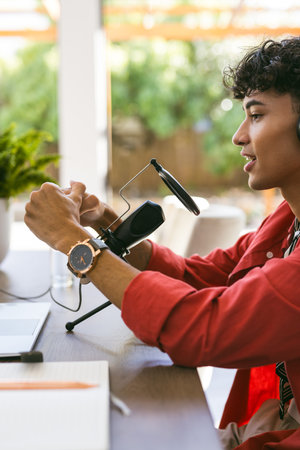 Using microphone and headphones, young man recording podcast at home workspace. home office, content creation, broadcasting, technology, audio, communicationの写真素材