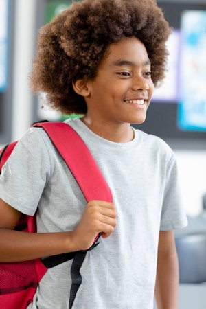 Vertical image of smiling african american schoolboy with afro, walking with schoolbag, copy space....