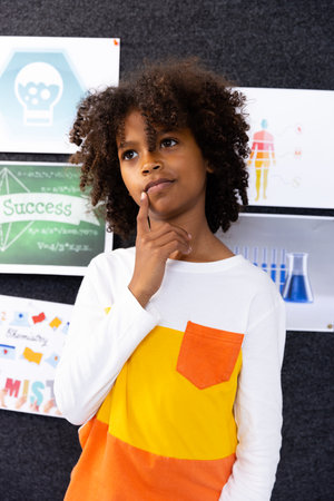 African american schoolboy in school classroom with chemistry posters in background. Education,...