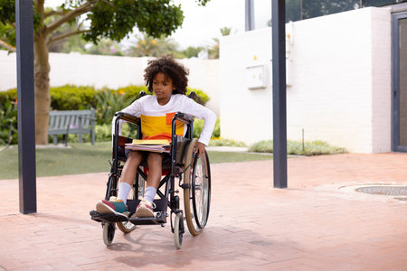 Happy african american schoolboy in wheelchair at school. Education, inclusivity, elementary school, learning and disability concept.の写真素材