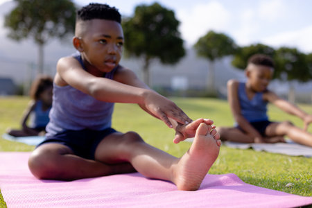 Happy african american schoolchildren doing yoga and stretching on field at school. Elementary school, sports, education and learning concept.の写真素材