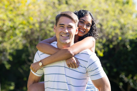 Smiling young couple enjoying piggyback ride outdoors in sunny park. Romance, happiness, playful, sunlight, love, carefreeの写真素材