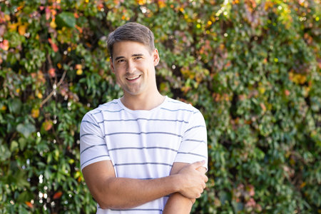 Smiling man in casual striped shirt standing outdoors with greenery background. Portrait, nature,...