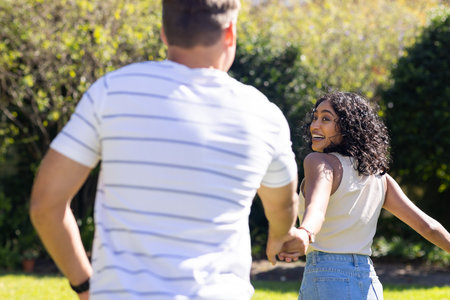 Holding hands, young couple enjoying playful moment outdoors in sunny park. Romance, love, summer, happiness, togetherness, relationshipの写真素材