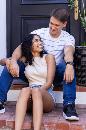 Smiling young couple sitting on steps, enjoying time together outdoors. happiness, togetherness, relationship, bonding, leisure, smilesの写真素材