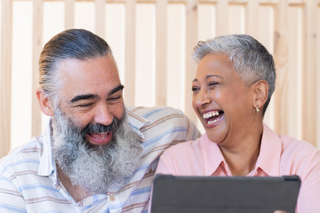Smiling senior couple using tablet and enjoying time together indoors. Technology, seniors, lifestyle, togetherness, happiness, bondingの写真素材