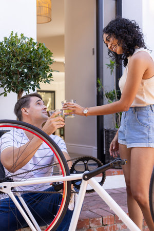 Fixing bicycle, young couple toasting with drinks, enjoying outdoor time together. Cycling, repairs, maintenance, teamwork, bonding, outdoorsの写真素材