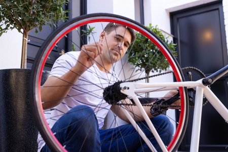 Repairing bicycle, man adjusting wheel spokes outdoors, focusing on maintenance. Cycling, mechanic, transportation, DIY, handyman, toolsの写真素材