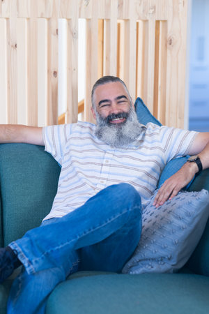 Smiling man with beard relaxing on couch, enjoying leisure time at home. Relaxation, indoors,...