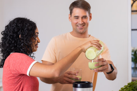 Pouring green smoothie into glasses, young couple enjoying healthy drink together. wellness, nutrition, lifestyle, fresh, detox, breakfastの写真素材