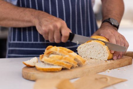 Slicing fresh bread on cutting board, person preparing meal in kitchen. Cooking, baking, homemade,...